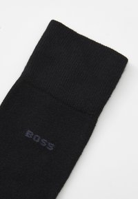 Fekete zokni bordázott anyagból, hajtott szegéllyel. Diszkrét "BOSS" logó sötétkék színben, a középen. Simára szőtt textúra, minta nélkül.