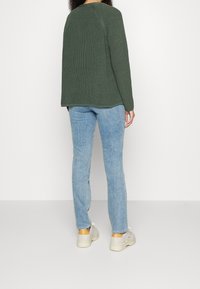 Green knit sweater with textured pattern, paired with light blue jeans and beige sneakers. The sweater has a rounded neckline and loose fit.