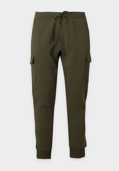 Σκούρα πράσινο cargo παντελόνι jogger με κορδόνι στη μέση, πλαϊνές τσέπες με καπάκι, ριμπ μανσέτες στους αστραγάλους και λεπτομέρειες ραφής στα γόνατα σε μονόχρωμο φόντο.