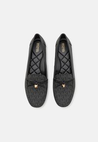 Sorte slip-on sko med et tekstureret stofoverdel, dekorativ sløjfe, guldfarvet logo-akcent og quiltet sort indvendig foring.