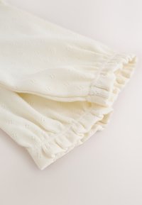 Close-up of soft white fabric with small knitted patterns and gathered elastic cuffs on sleeves.