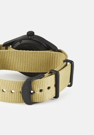 Juoda veido laikrodis su apvalia korpusu, chaki spalvos nailono dirželis ir plastikinis sagtis su skylutėmis pritaikymui. Timex prekės ženklas ant dirželio.