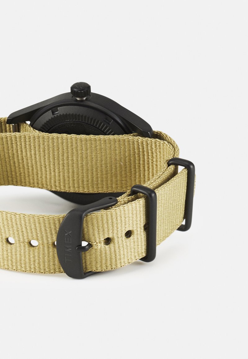 Schwarze analoge Uhr mit rundem Gehäuse, ausgestattet mit einem khakifarbenen Stoffarmband und schwarzer Hardware. Das Armband verfügt über mehrere Löcher zur Anpassung.