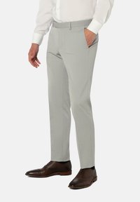 Pantalons taillés gris clair avec une texture lisse, coupe ajustée, poches latérales et une taille épurée, associés à des chaussures à lacets marron.