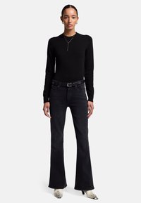 Maglione nero a maniche lunghe abbinato a jeans neri a zampa, accentuato da una cintura nera e tacchi con motivo pitonato. Design e vestibilità semplici.