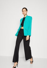 Blazer turquesa de corte relajado, combinado con un top corto negro y pantalones anchos negros. Tejido suave con bolsillos sutiles.