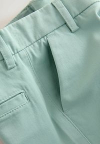 Pantalones cortos de algodón color teal claro con un frente plano, bolsillos laterales y trabillas para cinturón; presenta costuras visibles y una textura suave.