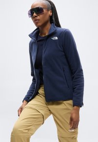 Ναυτικό fleece τζάκετ με φερμουάρ, ψηλό γιακά και πλαϊνές τσέπες. Συνδυάζεται με κάμπλε cargo παντελόνια. Διαθέτει λογότυπο στο αριστερό στήθος.