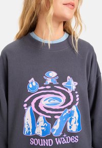 Sudadera gráfica en gris oscuro con una impresión colorida que presenta remolinos, montañas e íconos. Mezcla de algodón, corte relajado, escote de tripulación.