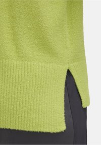 Pull en tricot de couleur vert lime vif avec une finition texturée, doté d'un ourlet côtelé et d'une fente sur le côté, associé à un tissu sombre en dessous.