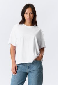 Weißes übergroßes T-Shirt mit kurzen Ärmeln, rundem Halsausschnitt und glatter Textur, kombiniert mit hellblauen Jeans.