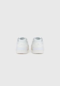 Adidași albi cu un exterior din piele netedă, guler căptușit și talpă din cauciuc texturat; branding minim pe partea din spate.