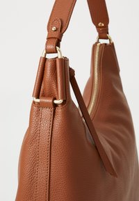 Braune Leder-Schultertasche mit strukturiertem Oberflächen, goldfarbenen Beschlägen und einem auffälligen Reißverschluss. Verfügt über einen breiten Tragegurt.