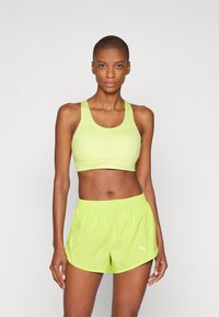 Sujetador deportivo verde claro con tirantes anchos y detalles texturizados, combinado con pantalones cortos sueltos a juego que cuentan con una cinturilla elástica y un logo.