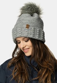 Berretto di maglia grigia con bordo a coste piegato e pon-pon in pelliccia sintetica sulla cima. Presenta un piccolo etichetta in pelle marrone sul lato.