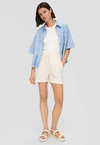 Lichtblauw shirt met korte mouwen over een wit T-shirt, gecombineerd met beige shorts en gevlochten sandalen. Eenvoudig ontwerp met een relaxte pasvorm.