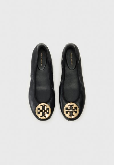 Ballerines en cuir noir avec un emblème rond en ton doré et un design découpé sur l'orteil. Texture lisse, style à enfiler.