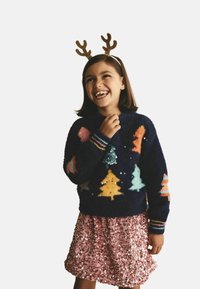 Knitted navy sweater with colorful tree designs and sequins; paired with a shiny pink sequin skirt. Girl wears glitter antlers.
