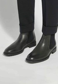 Black leather Chelsea boots with elastic side panels and a textured finish, featuring a low stacked heel and rubber outsole.