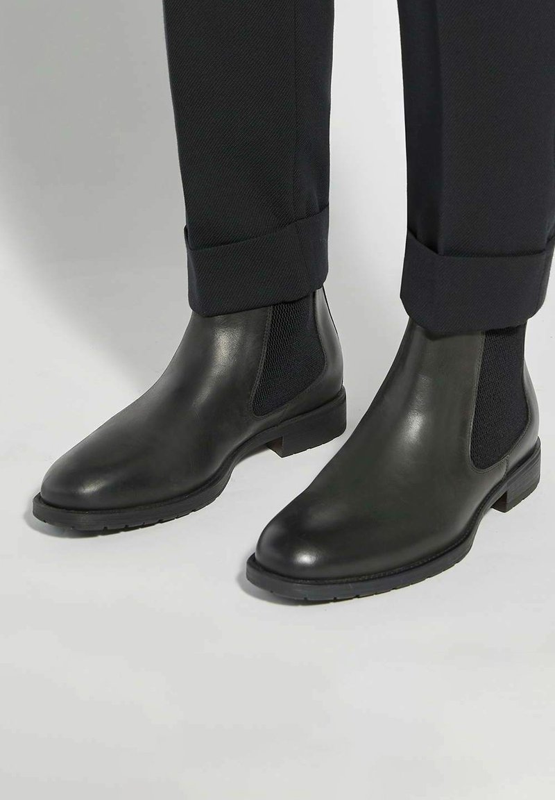 Black leather Chelsea boots with elastic side panels and a textured finish, featuring a low stacked heel and rubber outsole.