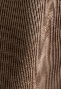 Brown corduroy fabric with vertical ribs, soft texture, and a consistent pattern, suitable for clothing or upholstery.