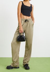 Czarny krótki top i beżowe, luźne spodnie dresowe z elastycznym pasem. Trzyma małą czarną torebkę o teksturowanej powierzchni. Czarne buty.