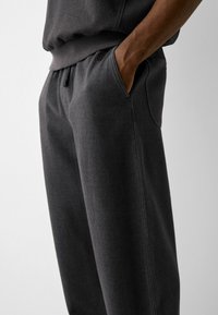 Tmavě šedé tepláky vyrobené z měkké směsi bavlny, s tahem v pase, bočními kapsami a jemnými švy.