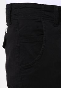 Svarta bomullsbyxor med raka ben, sidoficka och synliga sömmar på midjebandet och fickorna.