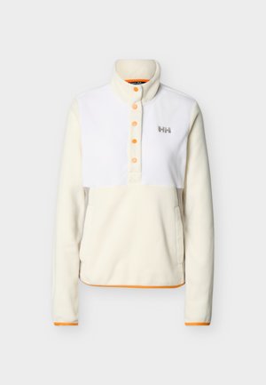 Kreemjasvalge fliisist pusa oranžide trukknappide, kõrge krae, küljetaskute, pikkade varrukate ja rinnal olev "HH" logoga.