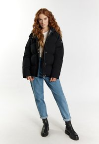 Zwarte pufferjas met een ritsluiting en logo-details. Gecombineerd met blauw jeans met opgerolde manchetten en zwarte enkellaarsjes.