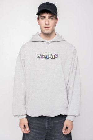 Grå hettegenser med lomme foran, prydet med fargerike blokkbokstaver som staver "kaotiko." Stoffet ser mykt ut og har en avslappet passform.