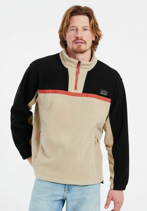 Fleece pullover in beige and black, featuring a half-zip with a red accent, side pockets, and a logo patch on the chest.