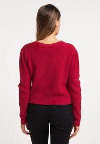 Röd stickad tröja med ribbat mönster, puff�ärmar och en scallopad krage. Matchad med svarta åtsittande byxor.