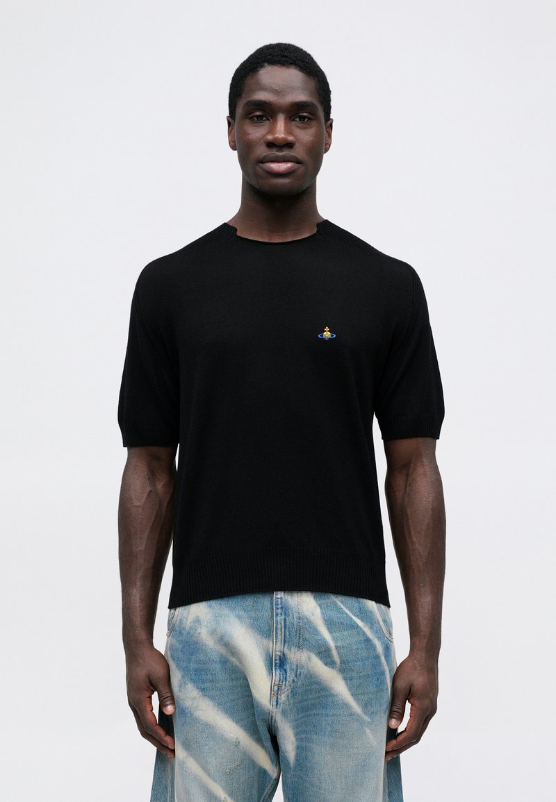 Maglione a maniche corte nero in maglia con dettagli a coste e un piccolo emblema ricamato. Abbinato a jeans azzurri a tie-dye.