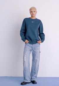 Sweatshirt Nike azul-marinho, ajuste descontraído, punhos canelados, combinado com jeans de perna larga desgastados em azul claro e sapatos robustos pretos.