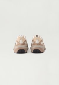 Sportskor med en beige och tan mockaexteriör med meshdetaljer, rundad design och en vadderad sula med texturerat svart mönster.