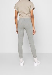 Leggings grises en un corte ajustado, hechos de una tela suave y elástica. Combinados con una camiseta corta beige y calzado blanco.
