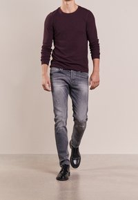 Ciemnofioletowa koszula z długim rękawem w połączeniu z szarymi, postrzępionymi dżinsami oraz czarnymi butami na sznurowadła. Gładki materiał, dopasowany krój bez wzorów.