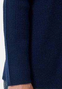 Dunkelblaues geribbeltes Strickpulloverärmel, der einen strukturierten Stoff mit deutlichen horizontalen Streifen aufweist. Die Bündchen sind leicht umgeschlagen.