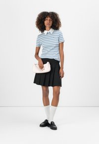 Polo a righe blu con colletto bianco, gonna plissettata nera, calze bianche sopra il ginocchio e mocassini neri. Gli accessori includono una pochette rosa.