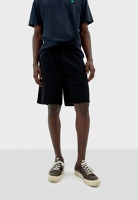 Shorts noirs texturés avec une taille élastique, associés à un t-shirt bleu marine foncé et des baskets marron avec des lacets blancs et des semelles crème.
