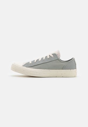 Low-top sneaker in grey fabric with white rubber sole, white laces, and speckled detailing on the sole, shown from the side on a white background.