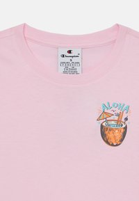 Világos rózsaszín pamut póló, melyen egy kókuszdió ital grafikája látható, rajta az "ALOHA" felirattal, szívószálakkal és egy kicsi ernyővel az elején.