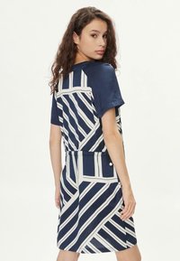 Abito blu navy con maniche corte, caratterizzato da un motivo geometrico bianco. Tessuto morbido e silhouette rilassata con un dettaglio in vita.