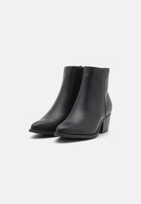 Bottes noires en cuir à hauteur de cheville, avec un bout pointu et un talon bas empilé. Texture lisse, sans motifs ni détails métalliques visibles.