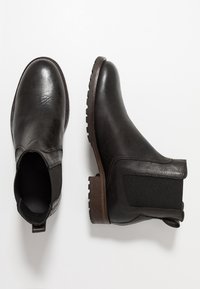 Bottes cheville en cuir noir avec panneaux latéraux élastiques et semelle extérieure texturée. Talon plat en bois, finition lisse avec un subtil détail de grain.