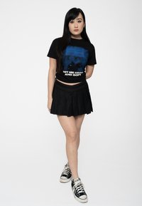 Black graphic t-shirt with blue design and white text, paired with a black pleated skirt and black high-top sneakers.