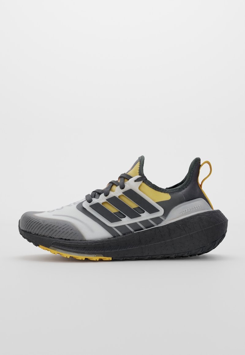 Chaussure de course Adidas noire, blanche et jaune avec une semelle épaisse noire et trois bandes noires sur le côté, vue en profil droit.