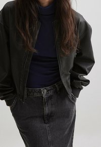 Chaqueta bomber de cuero negra con puños y cuello acanalados, combinada con un cuello alto azul marino y una falda de mezclilla oscura de talle alto. Tejido texturizado.