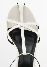 Sandal con tacco grigio chiaro caratterizzata da una parte superiore in pelle liscia, cinturini incrociati e una soletta in pelle nera con punta rotonda.